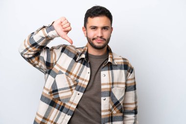 Beyaz arka planda izole edilmiş genç Brezilyalı adam olumsuz ifadeyle baş parmağını aşağı gösteriyor.