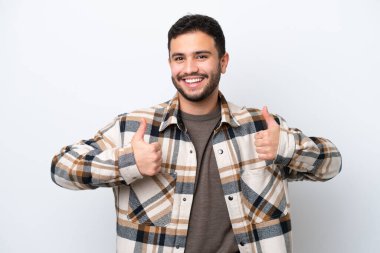 Beyaz arka planda izole edilmiş genç Brezilyalı bir adam baş parmak hareketi yapıyor.