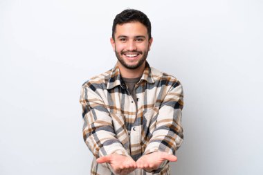 Beyaz arka planda izole edilmiş genç Brezilyalı bir adam bir ilan vermek için avucunun içinde hayali bir mekan tutuyor.