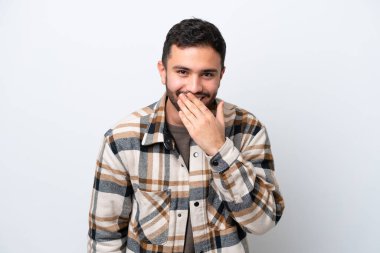 Genç Brezilyalı bir adam beyaz arka planda izole edilmiş mutlu ve gülümseyen ağızlarını eliyle kapatıyor.