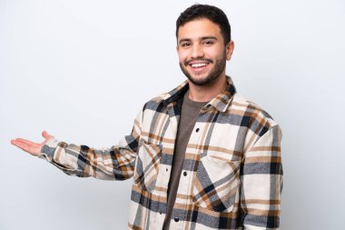 Beyaz arka planda izole edilmiş genç Brezilyalı adam, davet etmek için ellerini yana uzatıyor.