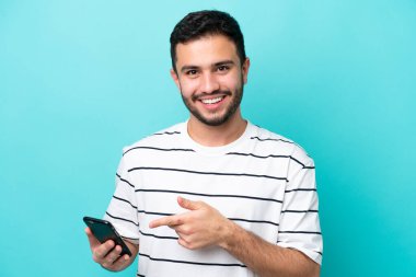 Genç Brezilyalı adam mavi arka planda cep telefonu kullanarak izole edilmiş.