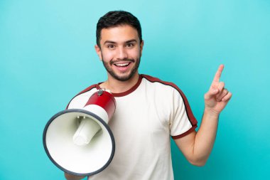 Mavi arka planda izole edilmiş genç Brezilyalı bir adam megafonla bağırıyor ve işaret ediyor.