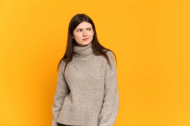Sarı arka planda izole edilmiş genç Ukraynalı kız yukarı bakarken şüpheleri var.