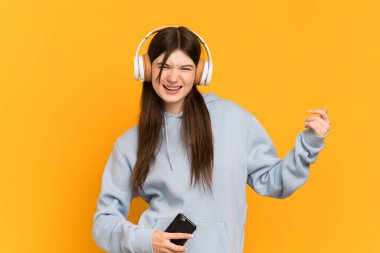 Genç Ukraynalı kız sarı arka planda izole edilmiş müzik dinliyor ve gitar hareketi yapıyor.