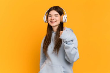 Genç Ukraynalı kız sarı arka planda izole edilmiş müzik dinliyor ve başparmağını kaldırıyor.
