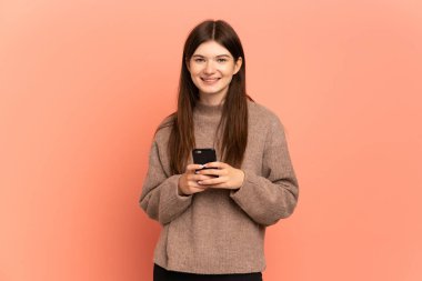 Pembe arka planda izole edilmiş genç Ukraynalı kız kameraya bakıyor ve cep telefonunu kullanırken gülümsüyor.