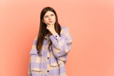 Pembe arka planda izole edilmiş genç Ukraynalı kızın şüpheleri ve kafa karıştırıcı bir yüz ifadesi var.