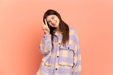 Pembe arka planda izole edilmiş genç Ukraynalı kız gülümsüyor ve zafer işareti gösteriyor.