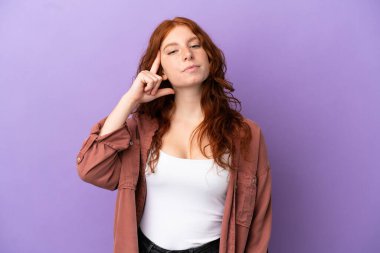 İzole edilmiş mor arka planda genç bir kızıl kız bir fikir düşünüyor.