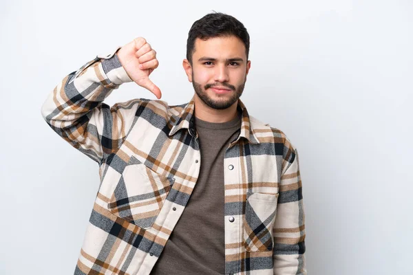 Beyaz arka planda izole edilmiş genç Brezilyalı adam olumsuz ifadeyle baş parmağını aşağı gösteriyor.