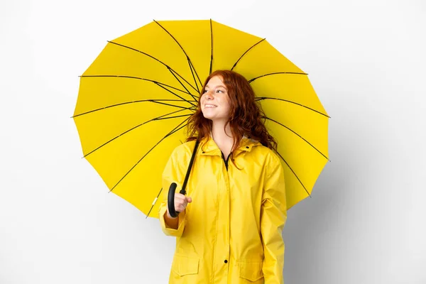 ティーンRedhead女の子レインプルーフコートと傘隔離上の白い背景考え方を考えながら上を見上げます — ストック写真