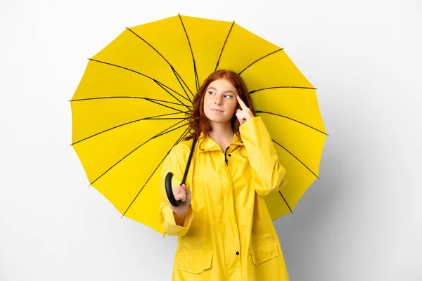 ティーンRedhead女の子レインプルーフコートと傘隔離上のホワイトバックグランド持って疑問と思考 — ストック写真