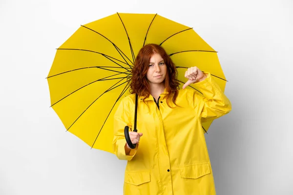 ティーンRedhead女の子雨防止コートと傘孤立上の白い背景ショー親指ダウンとともに負の式 — ストック写真