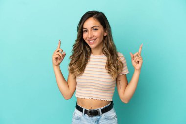 İzole edilmiş mavi arka planı olan genç bir kadın harika bir fikre işaret ediyor.