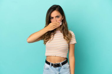 İzole edilmiş mavi arka plan, ağzı elle kaplayan genç bir kadın.