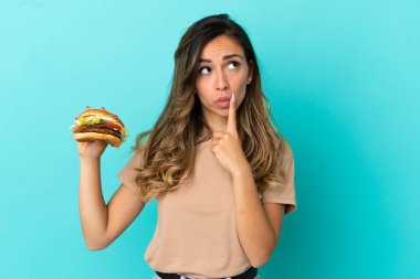 Arkaplanda hamburger tutan genç bir kadın yukarı bakarken şüphe duyuyor.