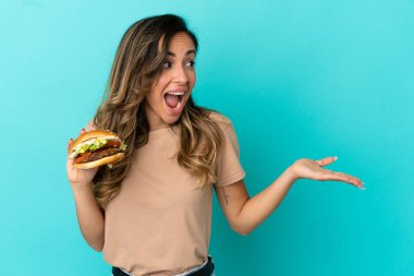 Arkaplanda hamburger tutan genç bir kadın. Sürpriz bir ifadeyle yan tarafa bakıyor.