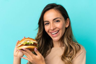 Arkaplanda hamburger tutan genç bir kadın.