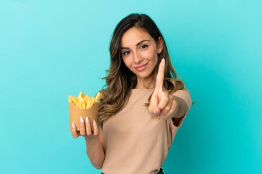 İzole edilmiş arka planda patates kızartması tutan ve parmağını kaldıran genç bir kadın.