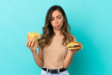 Arkaplanda kızarmış cips ve hamburger tutan genç bir kadın.