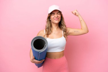 Genç sporcu kadın yoga derslerine giderken elinde minderle güçlü bir jest yapıyor.