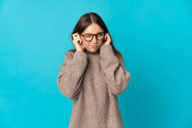 Genç Litvanyalı kadın mavi arka planda izole edilmiş hayal kırıklığına uğramış ve kulaklarını kapatmış