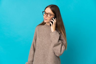 Genç Litvanyalı bir kadın mavi arka planda izole edilmiş. Cep telefonuyla biriyle sohbet ediyor.