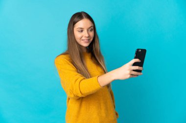 Genç Litvanyalı bir kadın mavi arka planda izole edilmiş ve selfie çekiyor.