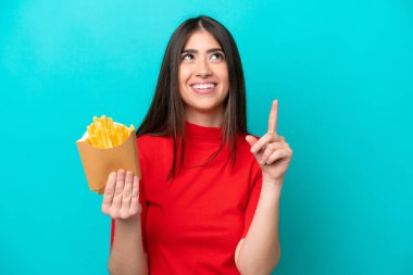 Mavi arka planda izole edilmiş patates kızartması yakalayan beyaz bir kadın harika bir fikre işaret ediyor.
