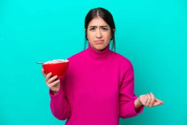 Mavi arka planda bir kase mısır gevreği tutan beyaz bir kadın, omuzlarını kaldırırken şüpheyle hareket ediyor.