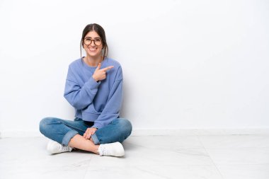 Beyaz arka planda izole bir şekilde yerde oturan beyaz saçlı genç bir kadın...