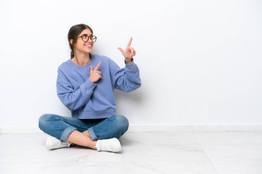 Beyaz arka planda izole bir şekilde yerde oturan genç beyaz kadın işaret parmağıyla işaret etmek harika bir fikir.