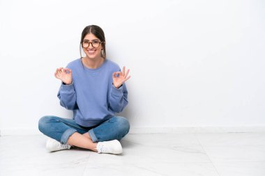 Beyaz arka planda izole bir şekilde yerde oturan genç beyaz kadın parmaklarıyla 