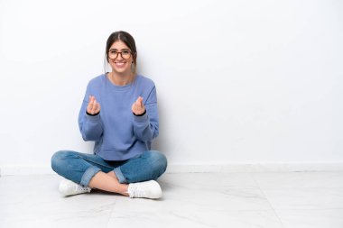 Beyaz arka planda izole bir şekilde yerde oturan beyaz bir kadın para hareketi yapıyor.