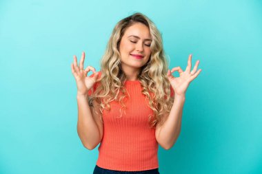 Genç Brezilyalı kadın Zen pozunda mavi arka planda izole edilmiş.