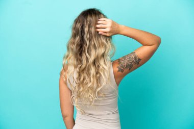 Genç Brezilyalı kadın mavi arka planda izole edilmiş ve düşünüyor.