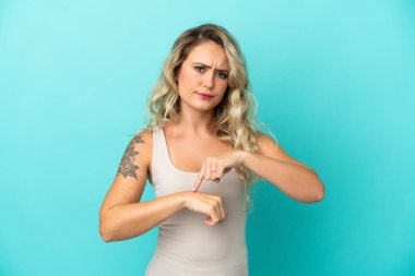 Mavi arka planda izole edilmiş genç Brezilyalı kadın geç kalma jesti yapıyor.