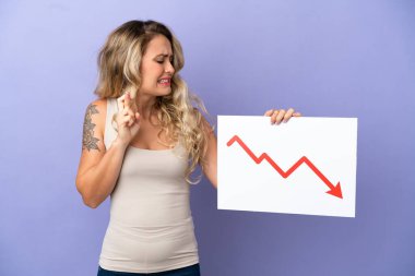 Mor arka planda izole edilmiş genç Brezilyalı bir kadın azalan bir istatistik okuyla işaret tutuyor ve parmaklarını çapraz yapıyor.