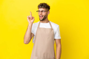 Restoran garsonu sarı arka planda izole edilmiş sarışın adam çözümü fark etmek için parmağını kaldırıyor.