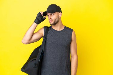 Spor çantalı genç sarışın adam sarı arka planda izole edilmiş. Şüpheleri var ve kafası karışık.