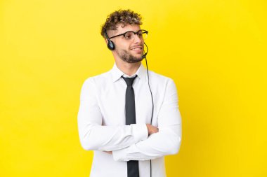 Tele pazarlamacı sarışın adam sarı arka planda izole edilmiş bir kulaklıkla çalışıyor mutlu ve gülümsüyor.