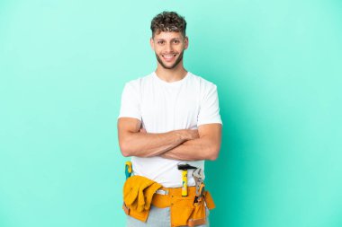 Young electrician blonde man isolated on green background keeping the arms crossed in frontal position