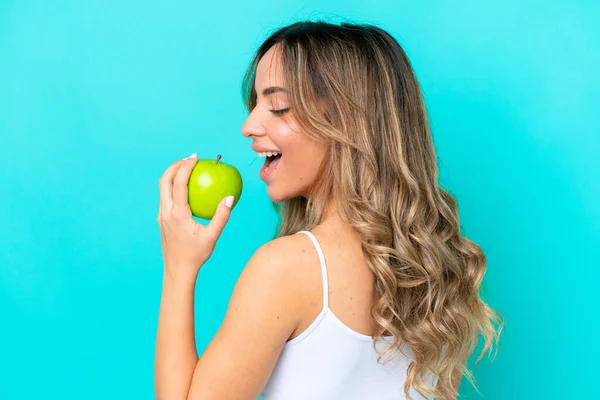 青の背景に隔離された若い白人女性がリンゴを食べる — ストック写真