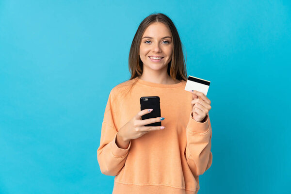 Young Lithuanian woman isolated on blue background buying with the mobile with a credit card