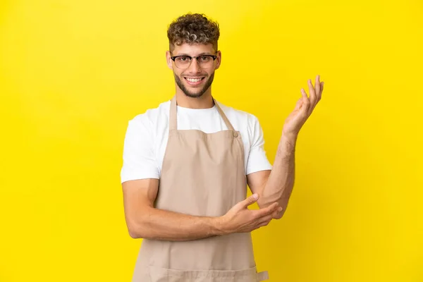 Restaurant Waiter Blonde Man Isolated Yellow Background Extending Hands Side — Zdjęcie stockowe