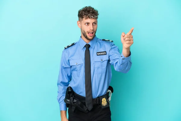 Young police blonde man isolated white on blue background pointing away