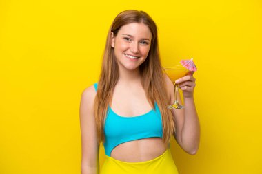 Sarı arka planda izole edilmiş bir kokteyl tutan beyaz bir kadın.