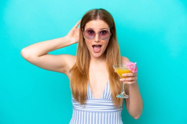 Mavi arka planda mayo giymiş ve elinde kokteyl tutan genç bir kadın.