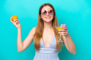 Mavi arka planda mayo giymiş ve elinde kokteyl tutan genç bir kadın.